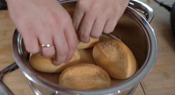 Das ausgeschnittene Backpapier in den Topf legen. Anschließend 4 Tiefkühlbrötchen in den Topf legen.