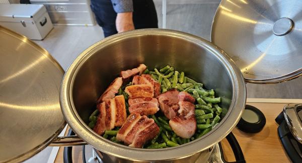 Das ganze nun mit dem Wasser ablöschen und die Gemüsebrühe einrühren, dann die Kartoffeln und Brechbohnen darauf geben und mit dem Bohnenkraut und Salz und Pfeffer würzen, nun die Speckscheiben wieder in den topf geben und den EasyQuick Smart auf den Topf setzten, den Navigenio auf stufe A ( Automatik ) drehen den Audiotherm ( Pieper ) auf den EasyQuick Smart setzten und die Dampfwolke einstellen sowie die erste Garzeit  6 Minuten. Wenn am Audiotherm ( Pieper ) ein Funk Symbolerscheint und am Navigenio das Blaue licht blickt ist alles richtig gemacht.